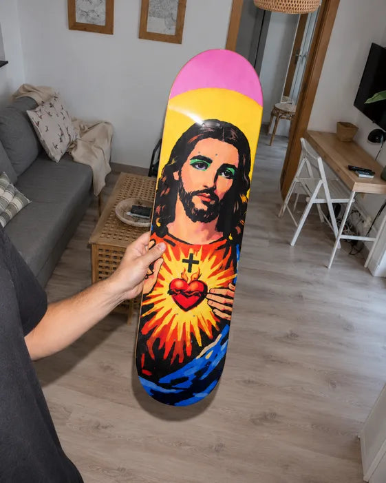 Hand holding a pop-art Sacred Heart skateboard deck in a bright living room